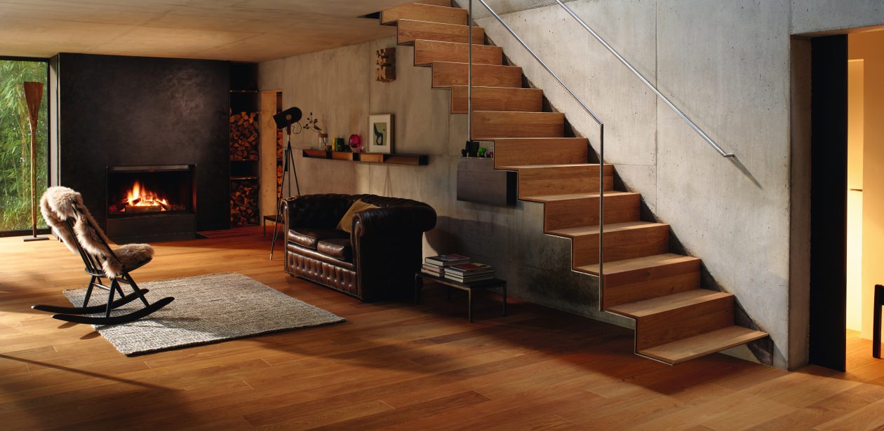 Modernes Wohnzimmer mit warmem HARO Parkettboden, der auch auf der Treppe verlegt ist.