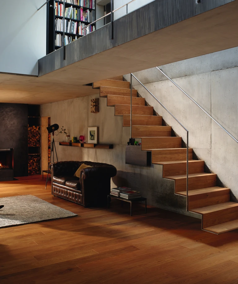 Modernes Wohnzimmer mit warmem HARO Parkettboden, der auch auf der Treppe verlegt ist.