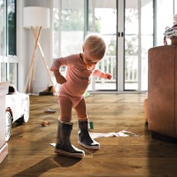 Niño pequeño con botas de goma sobre parquet HARO marrón: la curiosidad infantil se encuentra con un suelo resistente y acogedor.