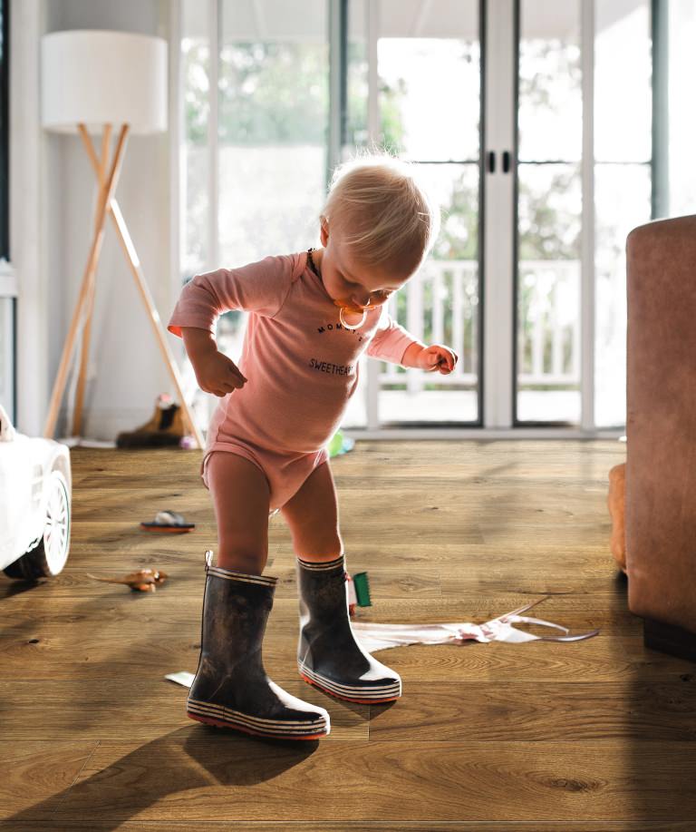 Small child in rubber boots on brown HARO parquet – childlike curiosity meets durable, homely flooring.