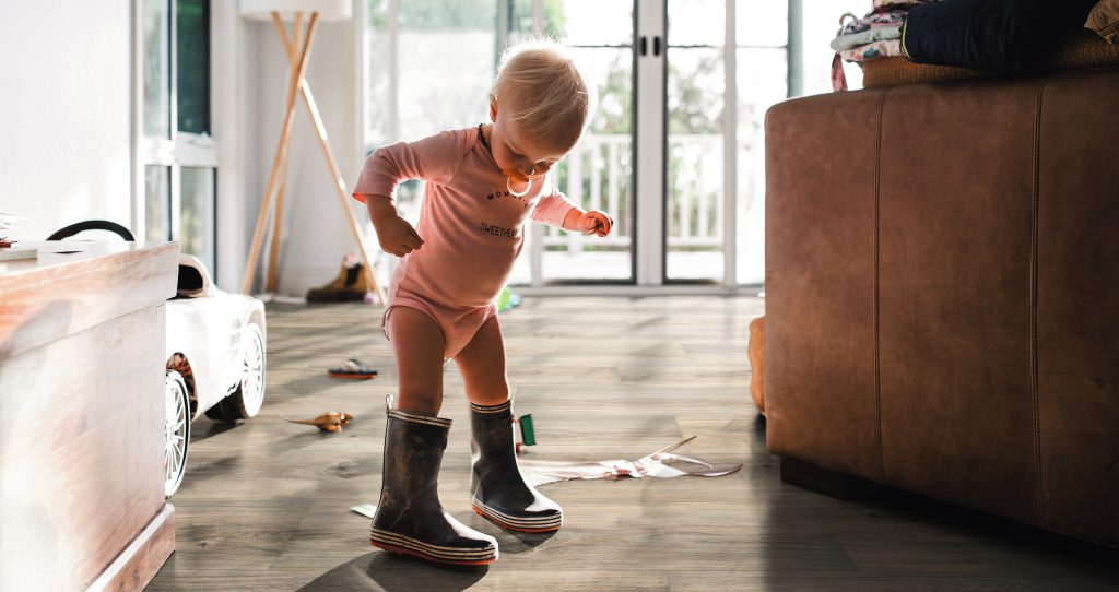 Kleines Kind in Gummistiefeln auf braunem HARO Parkett – kindliche Entdeckungsfreude trifft auf widerstandsfähigen, wohnlichen Bodenbelag.