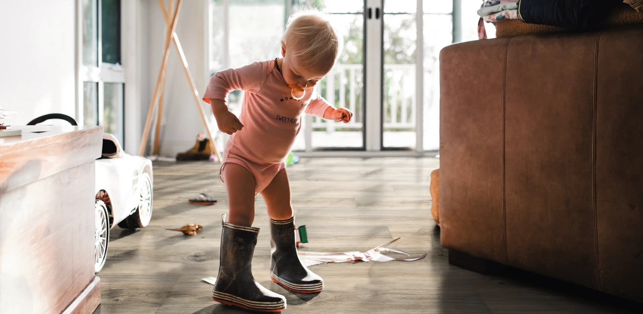 Kleines Kind in Gummistiefeln auf braunem HARO Parkett – kindliche Entdeckungsfreude trifft auf widerstandsfähigen, wohnlichen Bodenbelag.