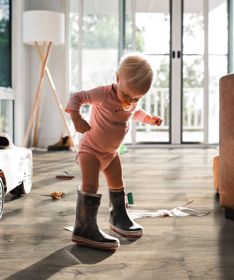 Kleines Kind in Gummistiefeln auf braunem HARO Parkett – kindliche Entdeckungsfreude trifft auf widerstandsfähigen, wohnlichen Bodenbelag.