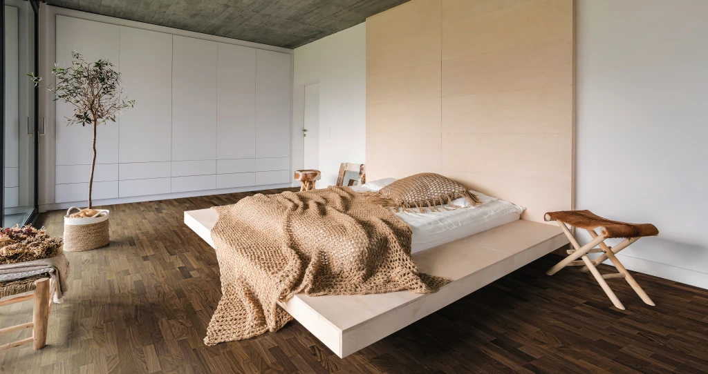 A cozy and warmly furnished bedroom with dark HARO parquet flooring, creating an elegant contrast to the bright interior.