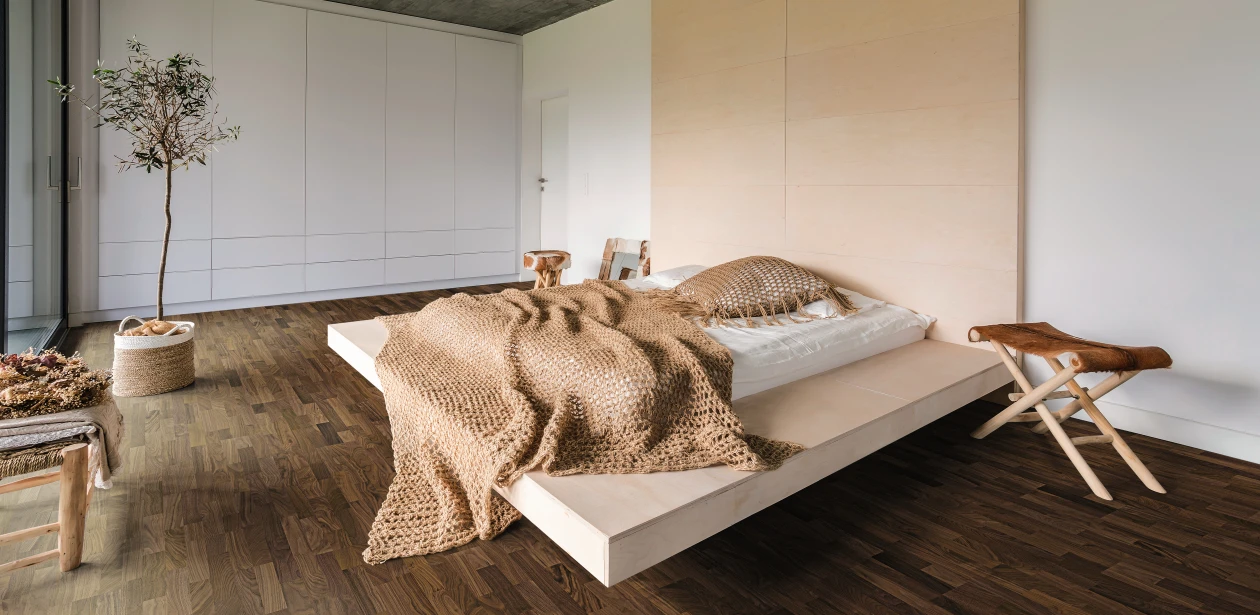 A cozy and warmly furnished bedroom with dark HARO parquet flooring, creating an elegant contrast to the bright interior.