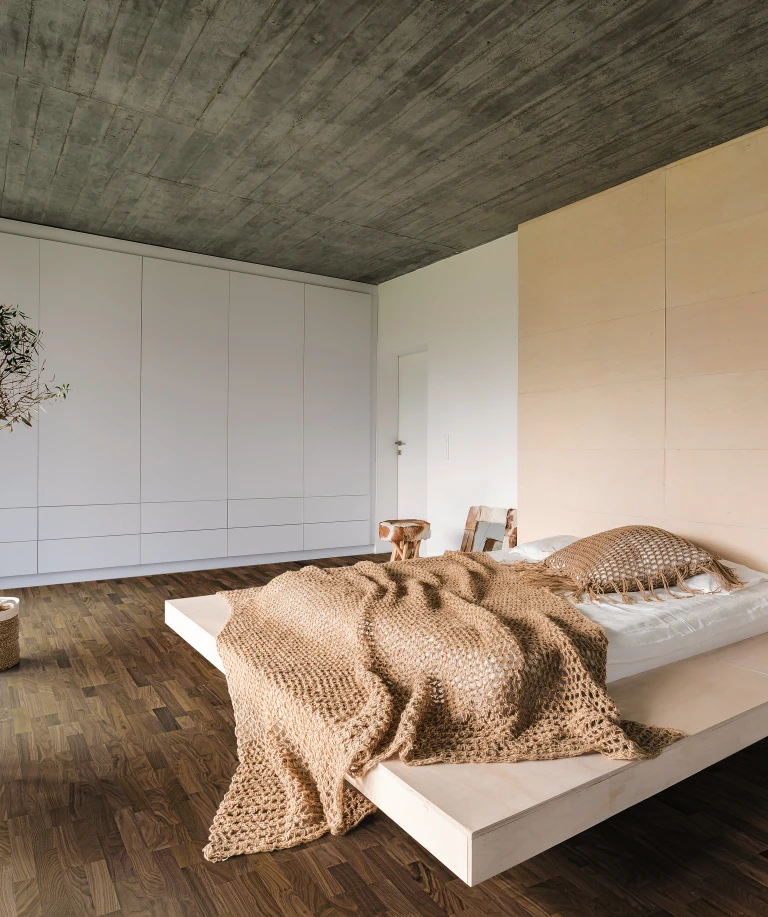A cozy and warmly furnished bedroom with dark HARO parquet flooring, creating an elegant contrast to the bright interior.