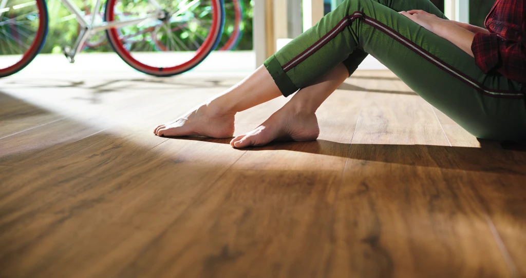 Eine Frau sitzt entspannt auf einem braunen HARO Designboden. Ihre nackten Füße berühren sanft die warme Oberfläche und unterstreichen die natürliche Gemütlichkeit des Raums.