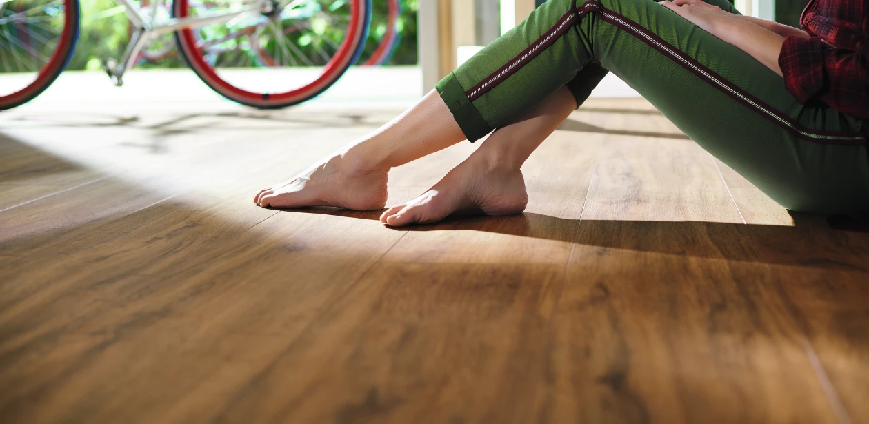 Eine Frau sitzt entspannt auf einem braunen HARO Designboden. Ihre nackten Füße berühren sanft die warme Oberfläche und unterstreichen die natürliche Gemütlichkeit des Raums.