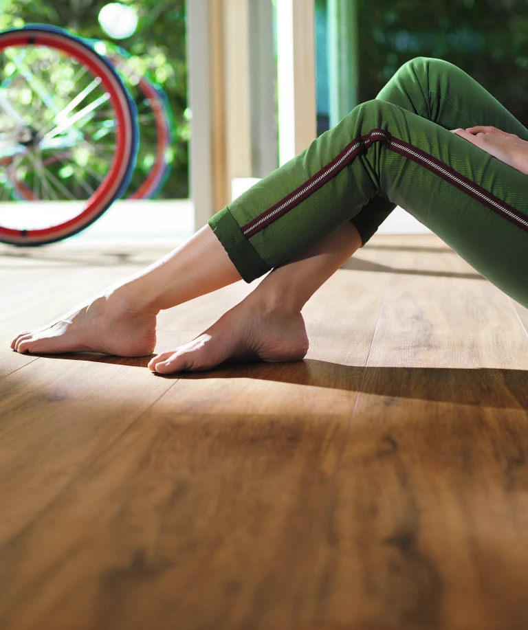 Eine Frau sitzt entspannt auf einem braunen HARO Designboden. Ihre nackten Füße berühren sanft die warme Oberfläche und unterstreichen die natürliche Gemütlichkeit des Raums.
