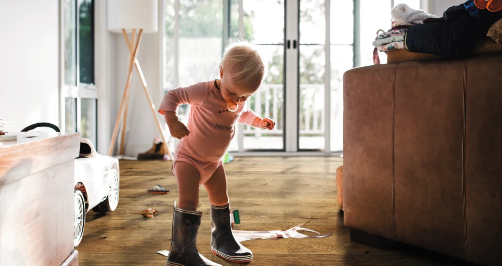 Kleines Kind in Gummistiefeln auf braunem HARO Parkett – kindliche Entdeckungsfreude trifft auf widerstandsfähigen, wohnlichen Bodenbelag.