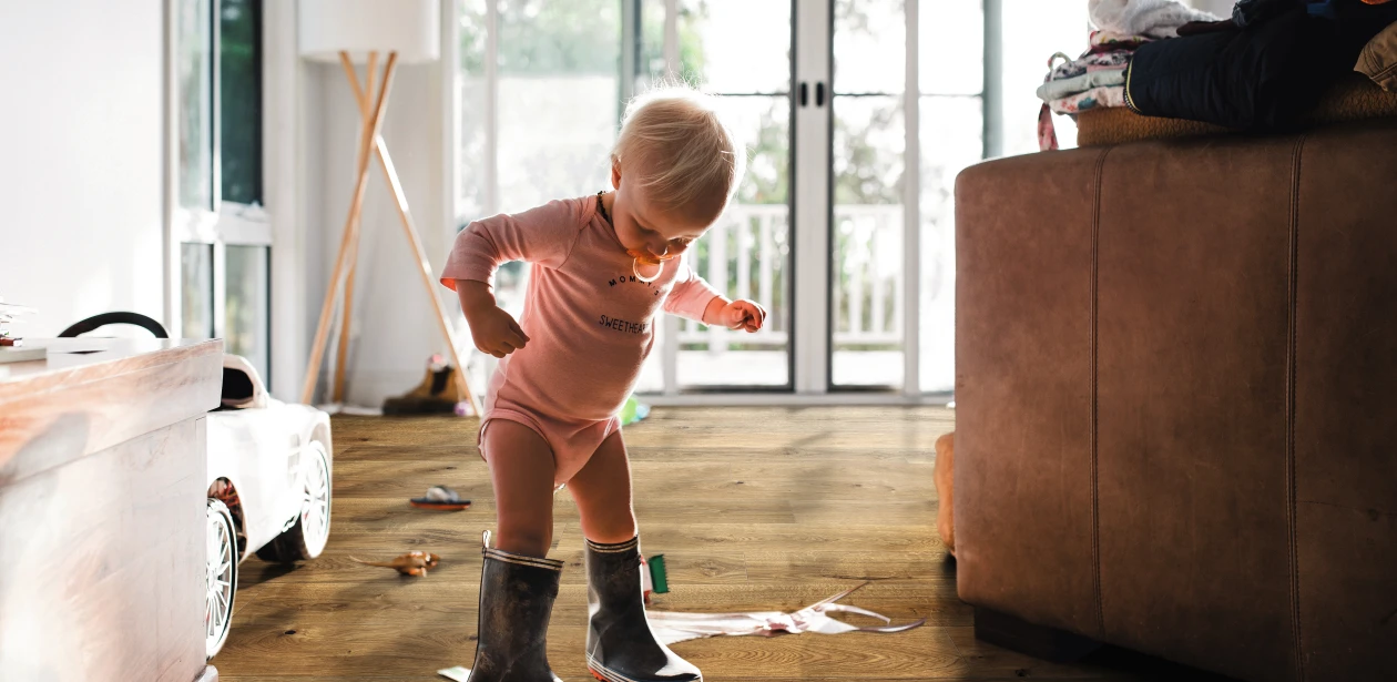 Kleines Kind in Gummistiefeln auf braunem HARO Parkett – kindliche Entdeckungsfreude trifft auf widerstandsfähigen, wohnlichen Bodenbelag.