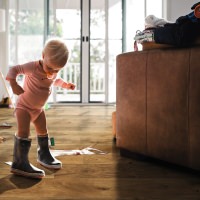 Niño pequeño con botas de goma sobre parquet HARO marrón: la curiosidad infantil se encuentra con un suelo resistente y acogedor.