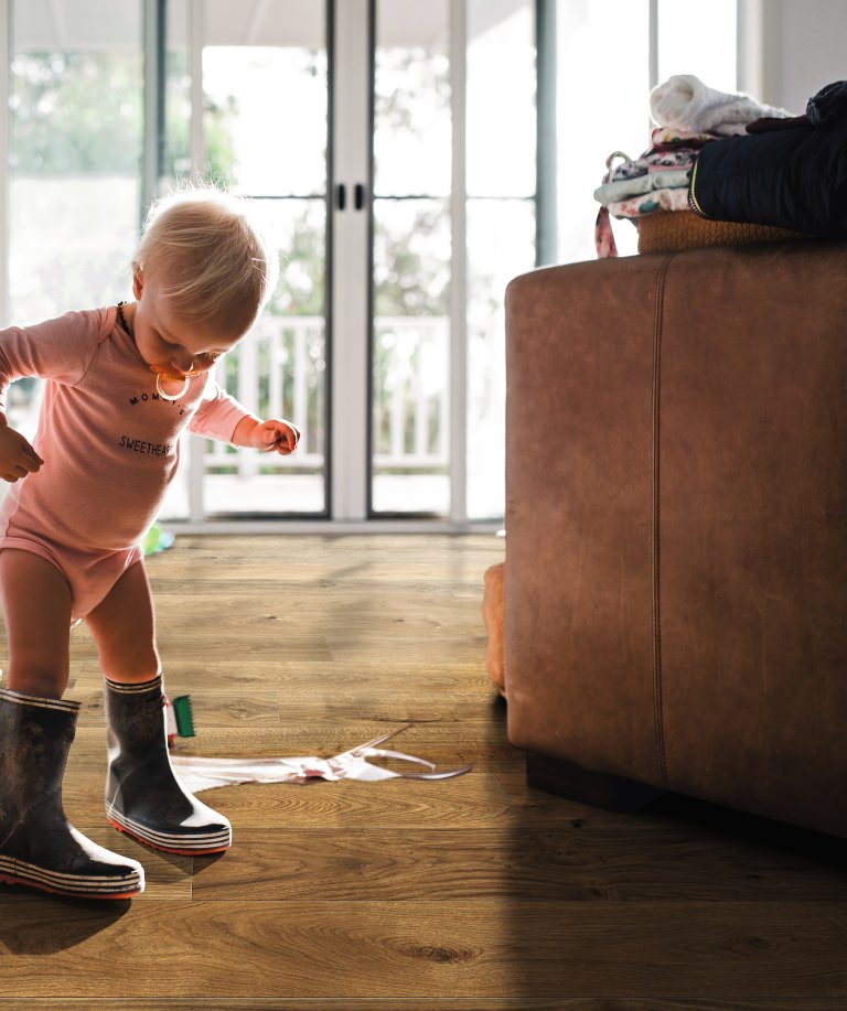 Kleines Kind in Gummistiefeln auf braunem HARO Parkett – kindliche Entdeckungsfreude trifft auf widerstandsfähigen, wohnlichen Bodenbelag.