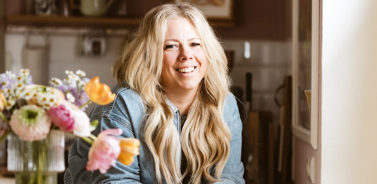 Die Influencerin Katharina Kammler steht mit einer Vase und einer Blume links neben ihr. Das elegante Arrangement unterstreicht eine stilvolle und harmonische Bildkomposition.