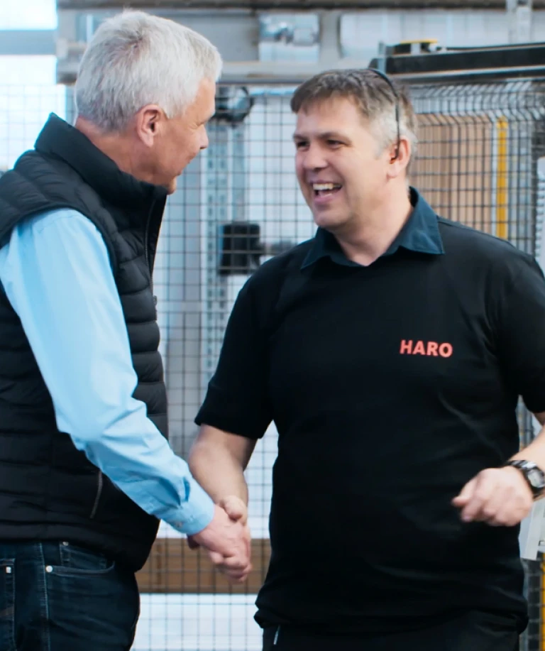 Zwei Männer stehen in einer Produktionshalle und schütteln sich die Hand – symbolisch für Zusammenarbeit, Vertrauen und den menschlichen Aspekt moderner Fertigung.