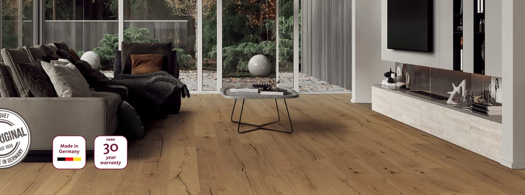 A modern living room with light HARO parquet flooring; a 'Made in Germany' seal, a 30-year guarantee symbol and a certificate of originality are visible in the bottom left-hand corner - an expression of quality, origin and durability.