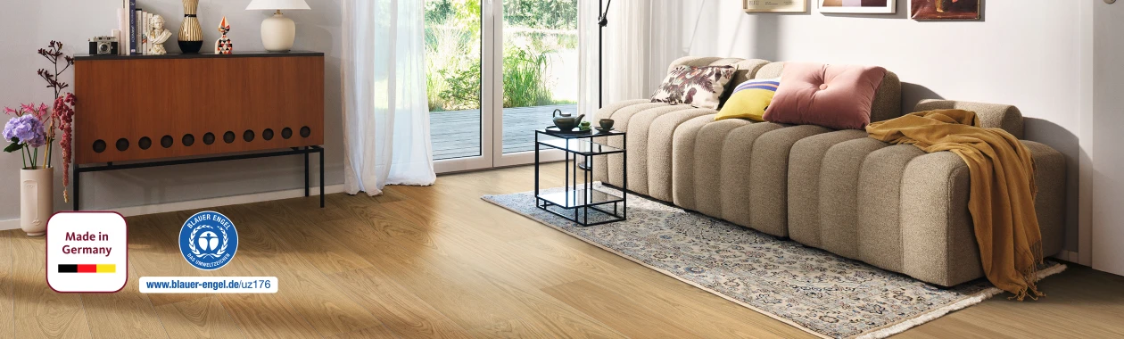 Cozy living room with a light brown HARO wood performance floor; furnished with a sofa and coffee table, bathed in natural daylight streaming generously from outside.