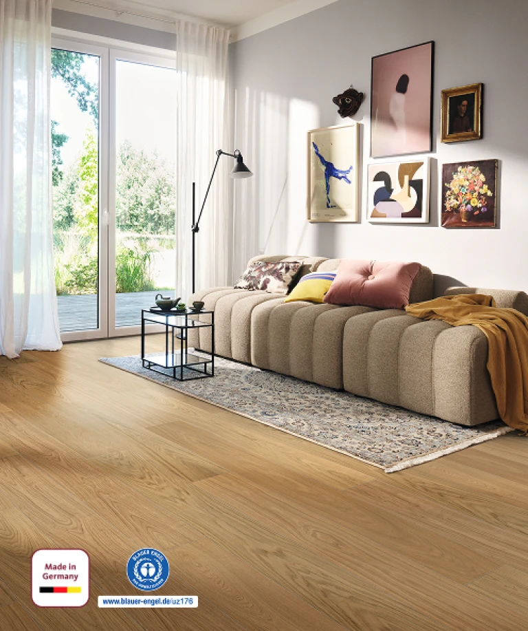 Cozy living room with a light brown HARO wood performance floor; furnished with a sofa and coffee table, bathed in natural daylight streaming generously from outside.