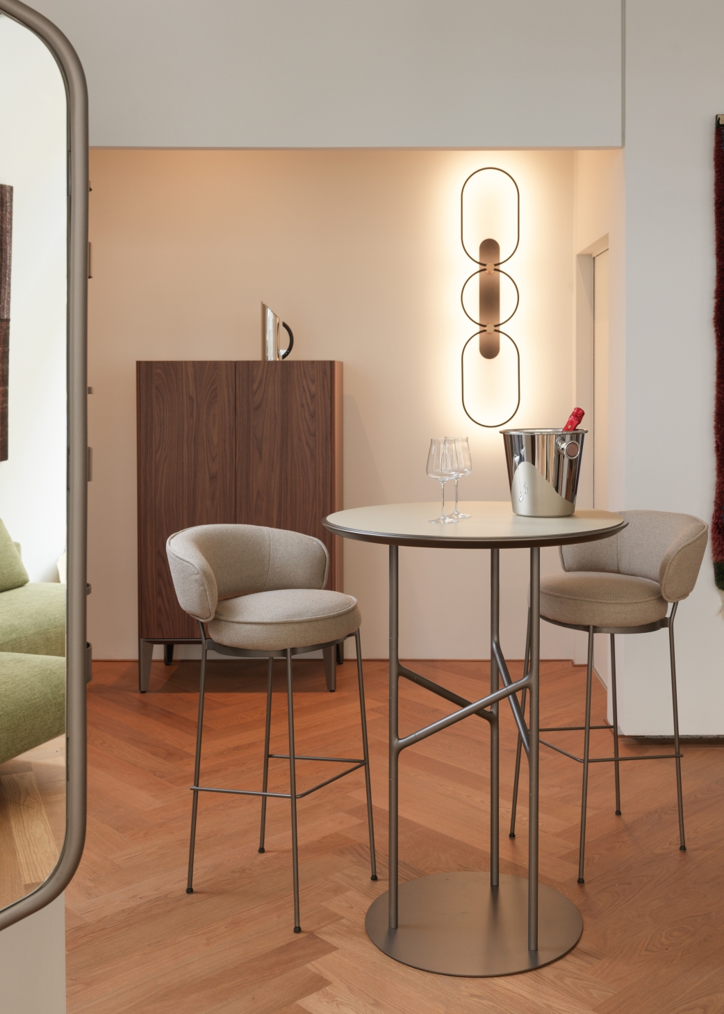 La imagen muestra una habitación decorada cálidamente con una mesa alta y dos taburetes. En el suelo se ha colocado un parquet HARO marrón oscuro en espiga.