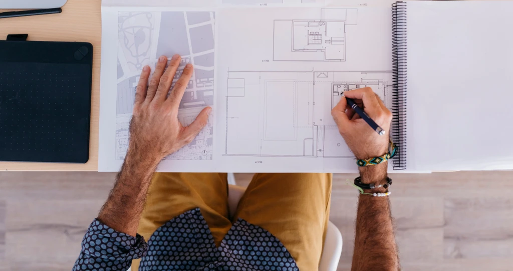 Mann zeichnet auf einem Raumplan – Planung und Berechnung von Bodenflächen.