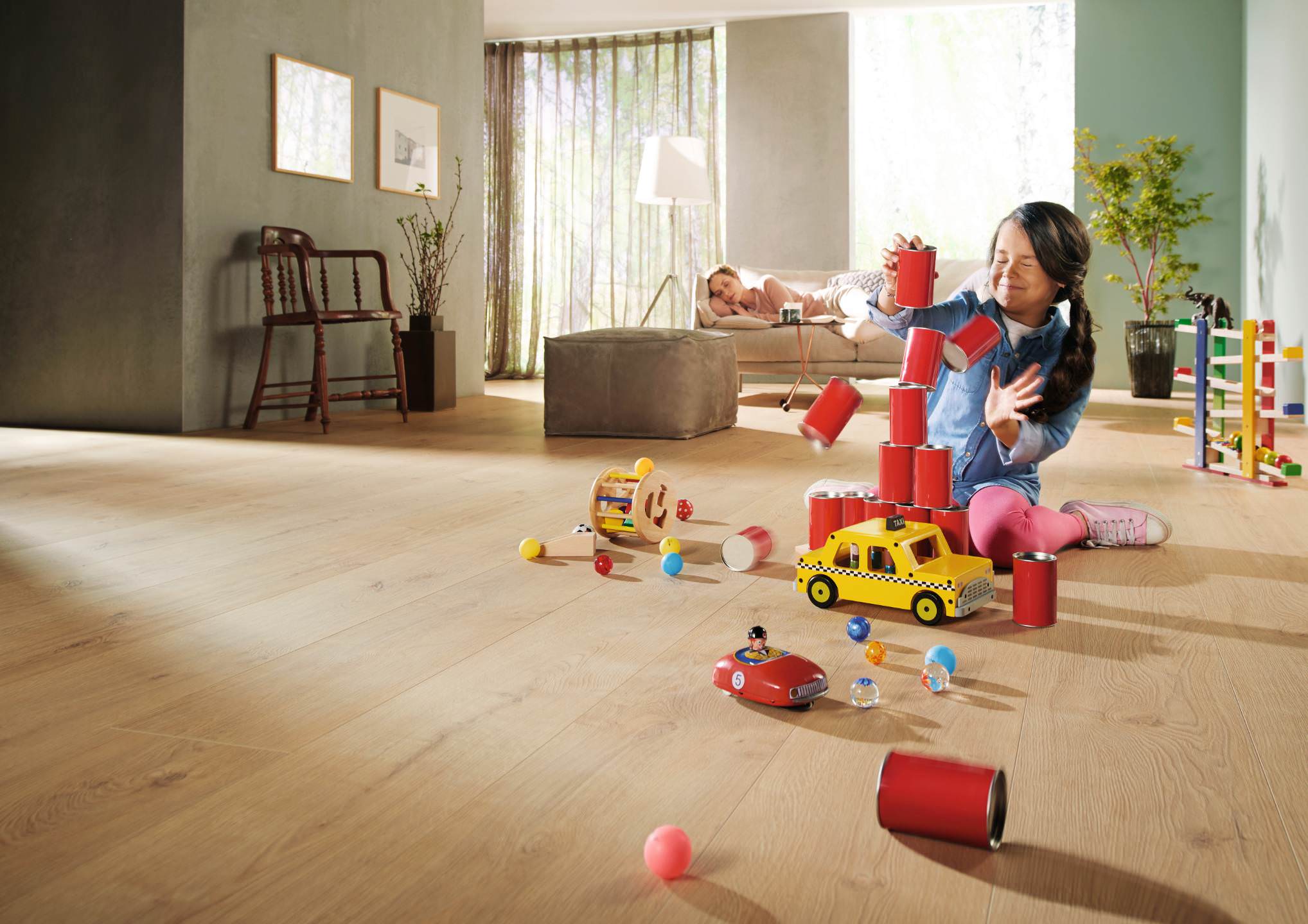Salon ouvert avec des accents vert foncé. Un enfant joue sur le sol en stratifié clair avec divers jouets, créant une atmosphère vivante et chaleureuse.