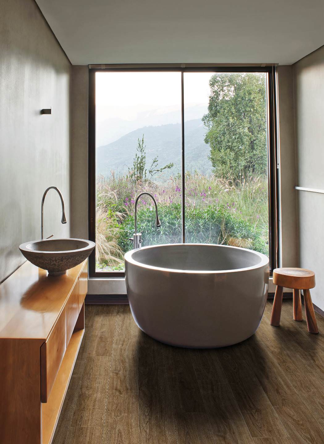 Salle de bain moderne avec une grande baie vitrée et un sol stratifié HARO brun. Une baignoire ronde et élégante est placée au centre, soulignant l’ambiance raffinée.