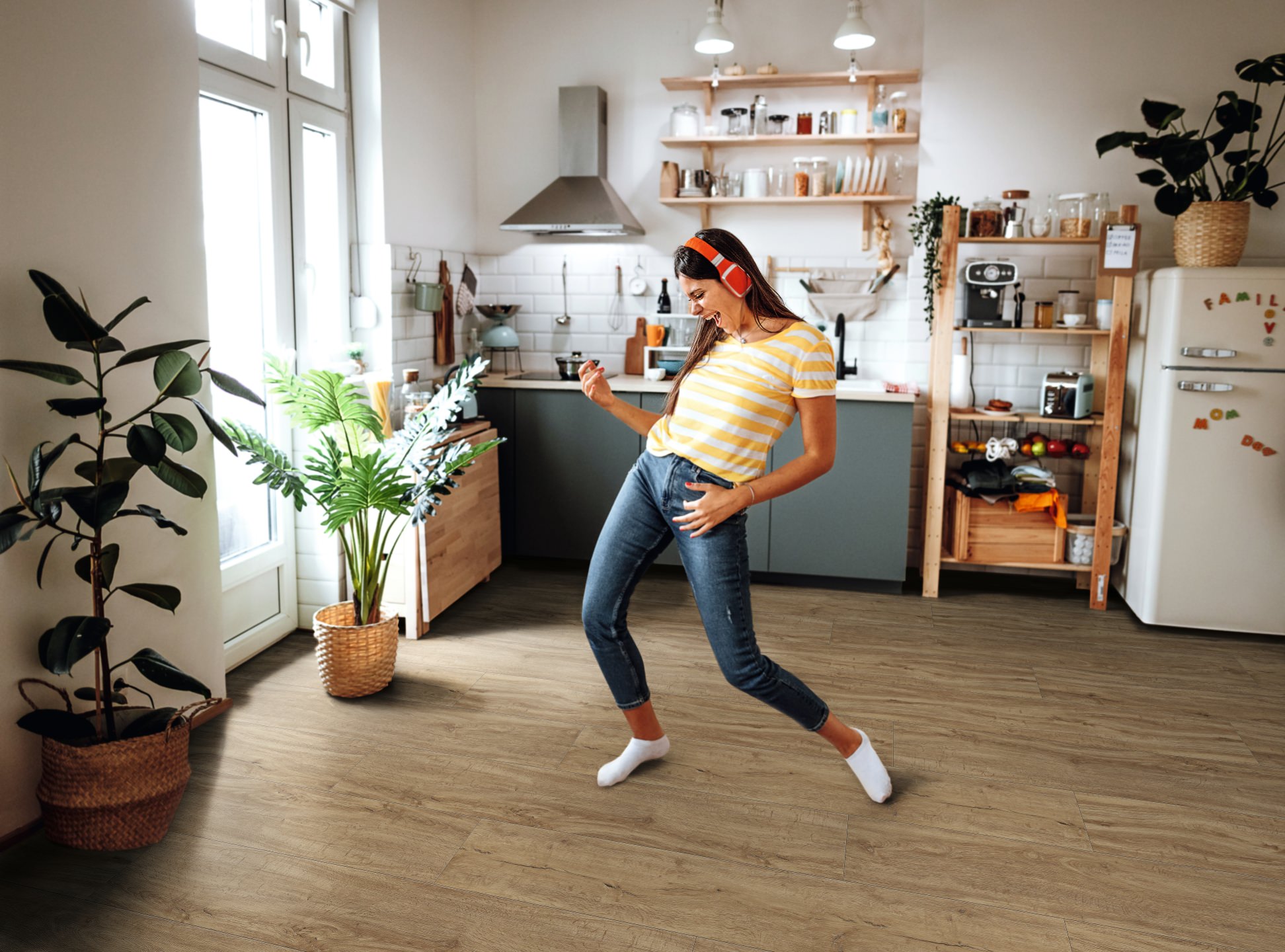 Cocina minimalista con suelo de diseño HARO marrón. En el centro de la habitación, una mujer disfruta de su música con auriculares y toca la guitarra aérea con entusiasmo.