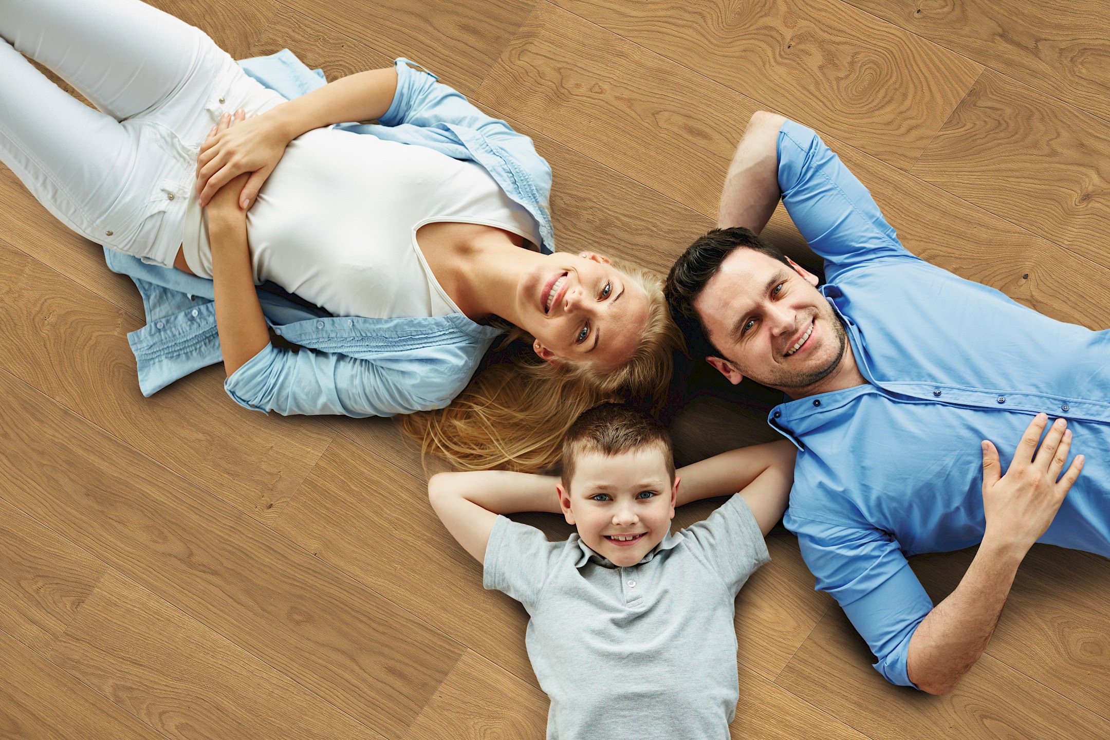 Une famille – mère, père et fils – est allongée tête contre tête sur un parquet HARO, profitant d’un moment de détente ensemble.
