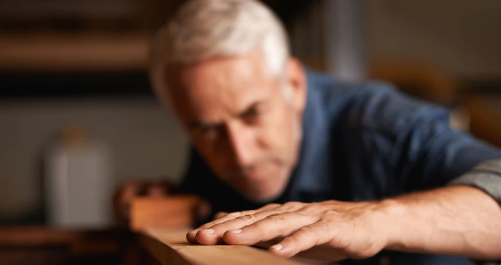 Ein Herr begutachtet konzentriert eine einzelne Diele – Ausdruck von Qualitätsbewusstsein, handwerklicher Präzision und dem Anspruch auf Perfektion im Detail.