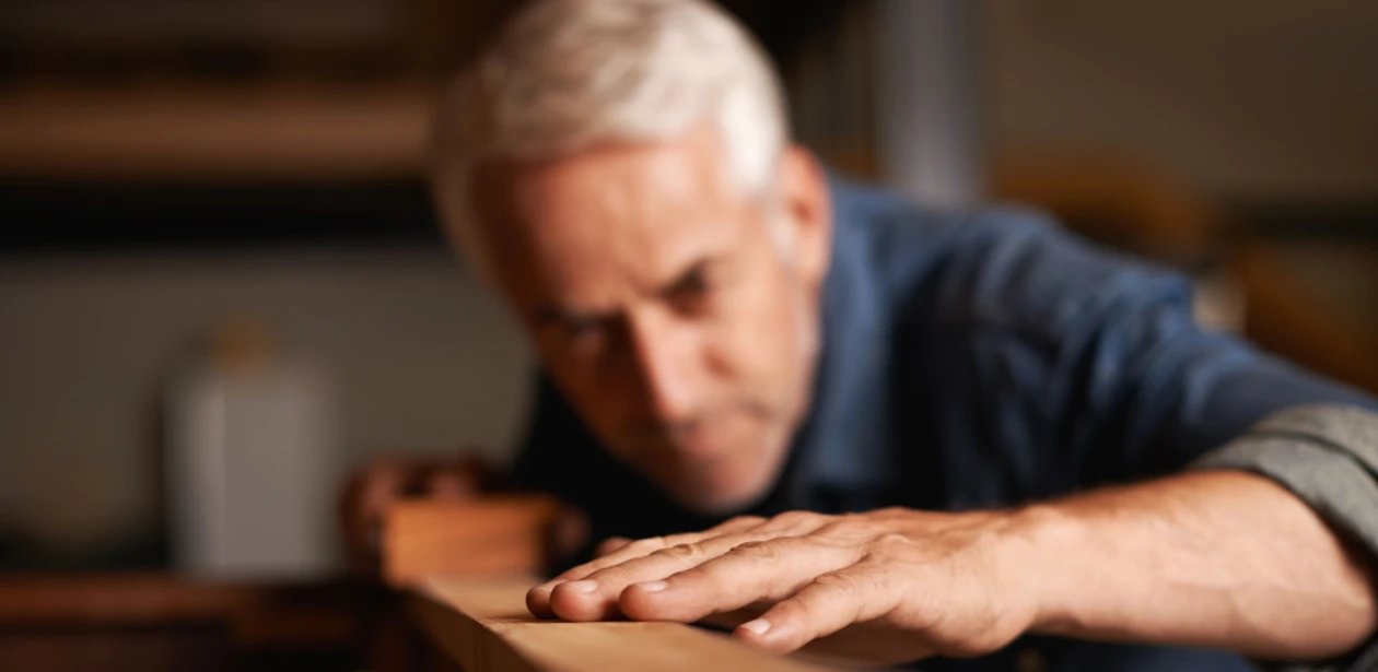 Ein Herr begutachtet konzentriert eine einzelne Diele – Ausdruck von Qualitätsbewusstsein, handwerklicher Präzision und dem Anspruch auf Perfektion im Detail.