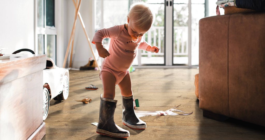 Kleines Kind in Gummistiefeln auf braunem HARO Laminat – kindliche Entdeckungsfreude trifft auf widerstandsfähigen, wohnlichen Bodenbelag.