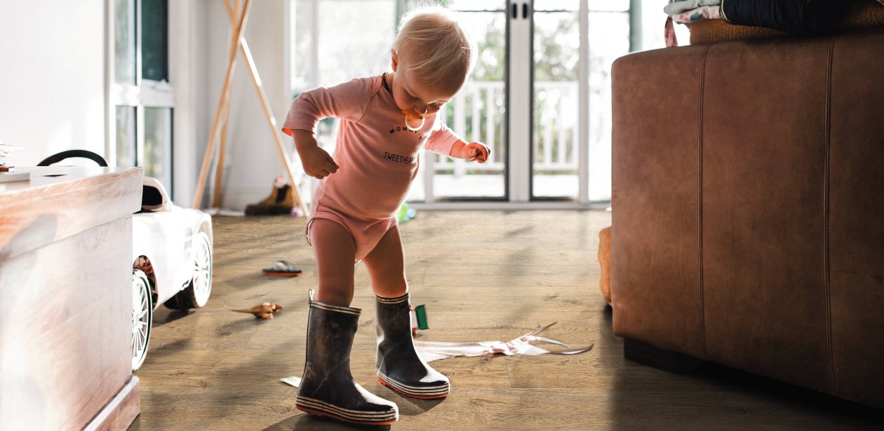 Kleines Kind in Gummistiefeln auf braunem HARO Laminat – kindliche Entdeckungsfreude trifft auf widerstandsfähigen, wohnlichen Bodenbelag.