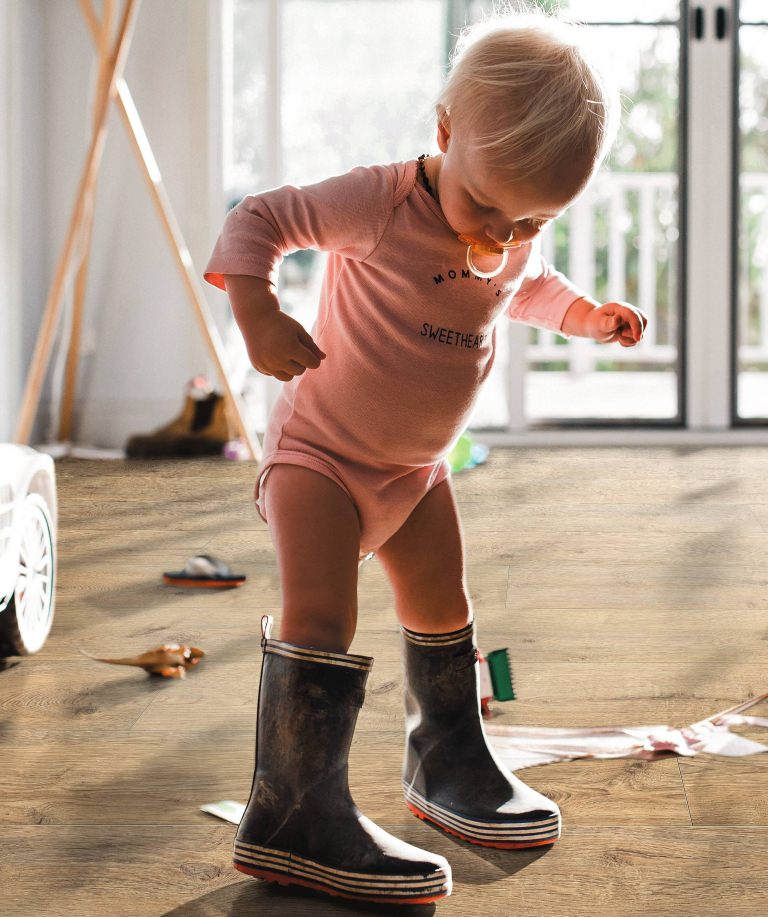 Kleines Kind in Gummistiefeln auf braunem HARO Laminat – kindliche Entdeckungsfreude trifft auf widerstandsfähigen, wohnlichen Bodenbelag.